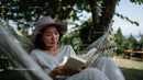 Woman Relaxing in Hammock Reading Under Green Trees on Summer Day