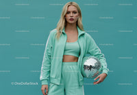 Young Woman in Mint Green Tracksuit Holding Disco Ball in Studio