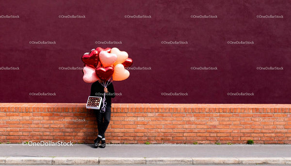 Person Holding Heart Balloons and Chocolates on Brick Wall