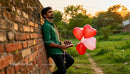 Man holding heart balloons and chocolates near brick wall