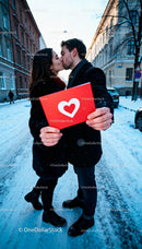Couple Sharing a Kiss Holding a Red Heart Card Outdoors
