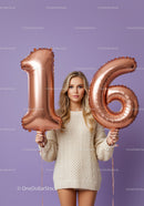 Young woman holding rose gold 16 balloons on purple background