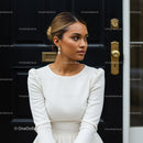 Elegant woman in white dress posing by dark door