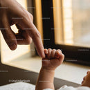 Tender moment of baby holding adult finger near window