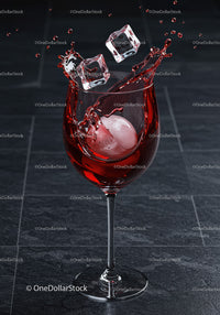 Red wine splash with ice cubes in glass on dark floor