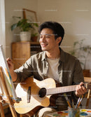 Man enjoying painting while holding acoustic guitar indoors
