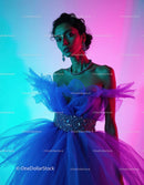 Elegant Woman in Blue Tulle Evening Gown with Jewelry Under Vibrant Lights