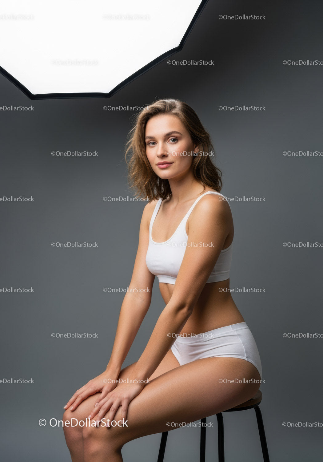 Elegant Young Woman Sitting on a Stool in a Studio with Soft Lighting