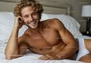 Smiling man with curly hair relaxing on white bed