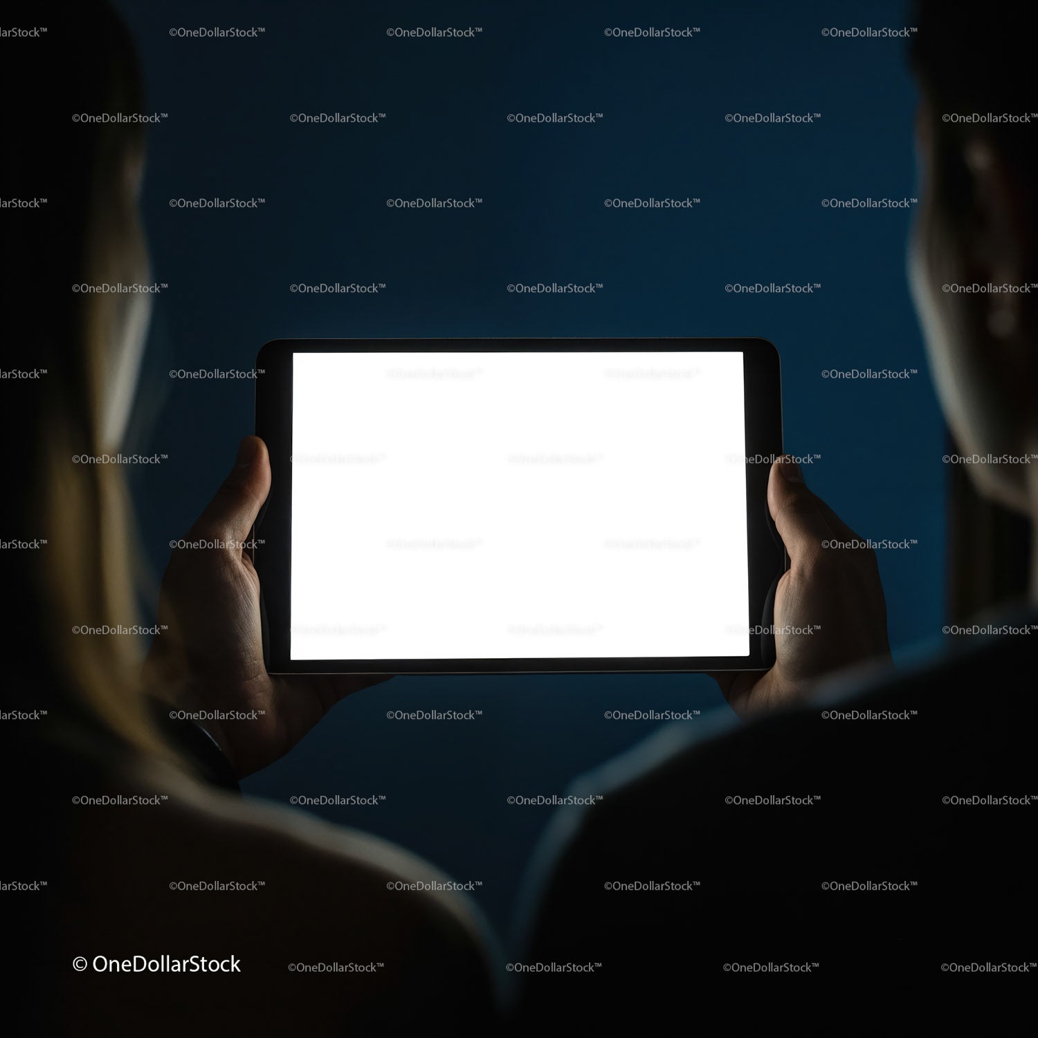 Two people viewing a lit digital tablet in darkness