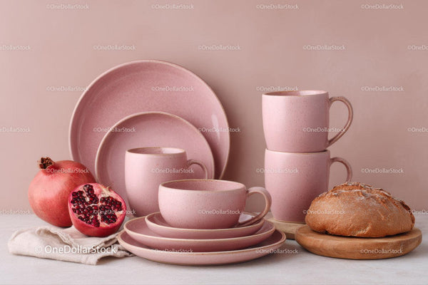 Różowe ceramiczne filiżanki i talerze z świeżym granatem i chlebem