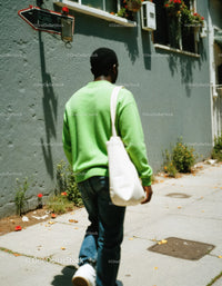 Young Man Walking on City Sidewalk in Casual Green Sweatshirt and Jeans