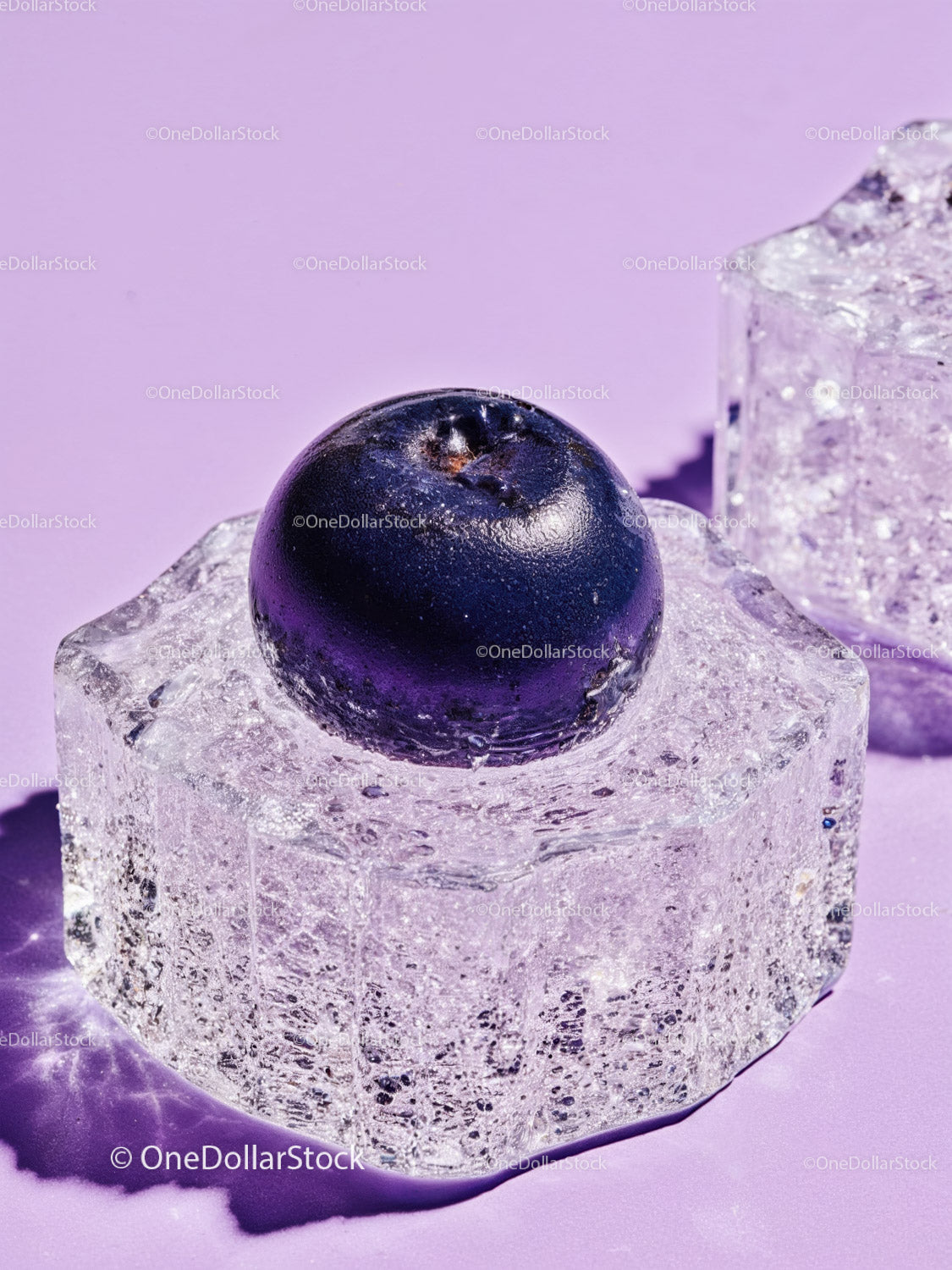 Fresh blueberry resting on clear ice cube on lavender surface
