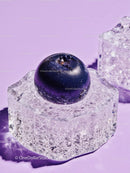 Fresh blueberry resting on clear ice cube on lavender surface
