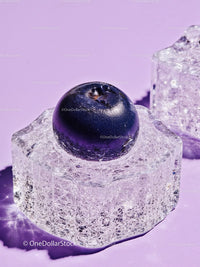 Fresh blueberry resting on clear ice cube on lavender surface