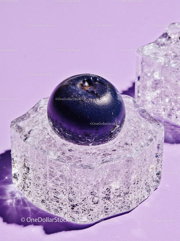 Fresh blueberry resting on clear ice cube on lavender surface