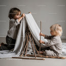 Two young children building an indoor stick and cloth tent