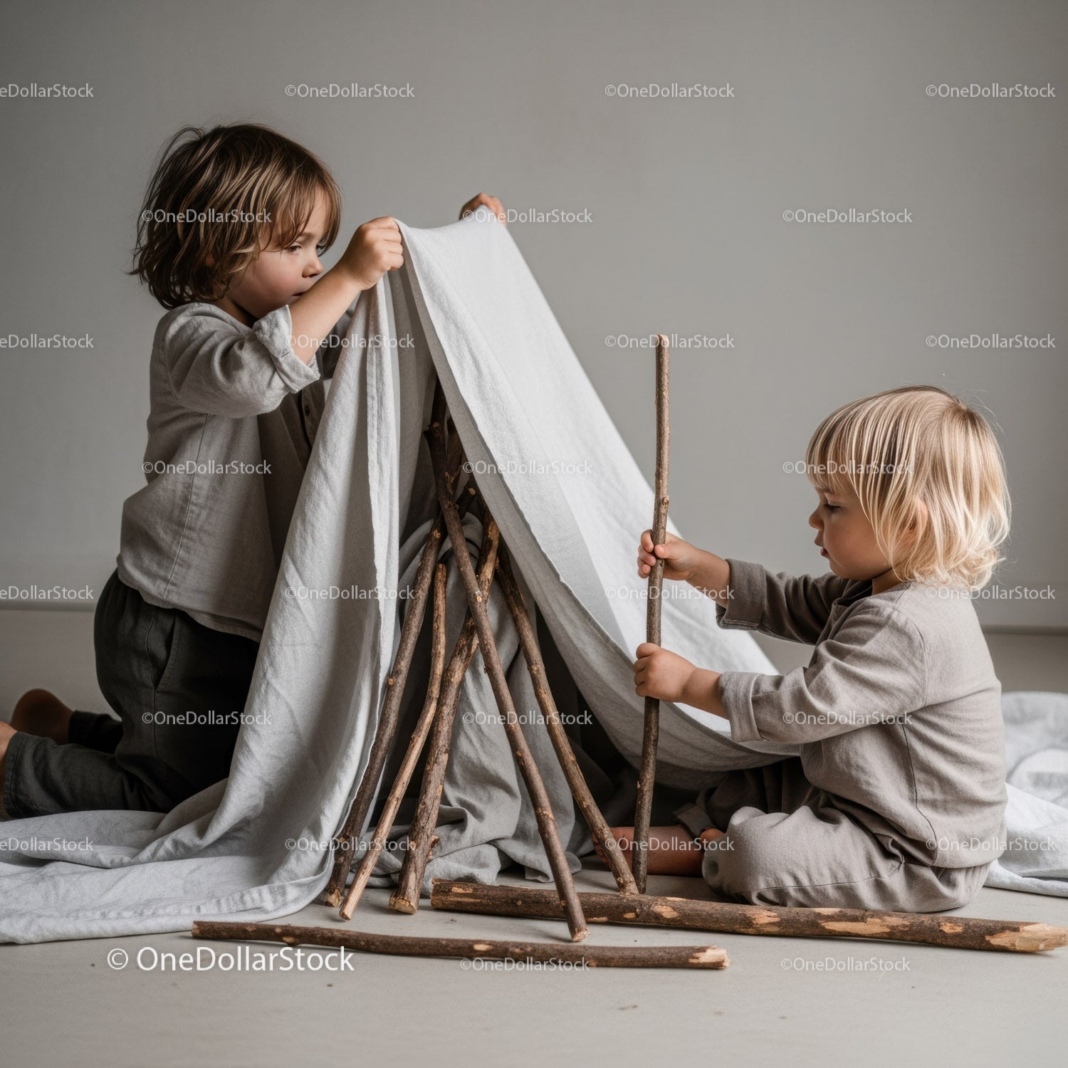 Two young children building an indoor stick and cloth tent