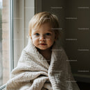 Cute toddler wrapped in soft beige blanket by window