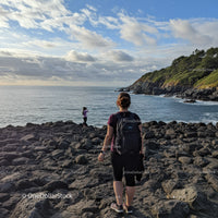 Women Hiking Along Rocky Seaside Coast with Green Hills Under Scenic Sky