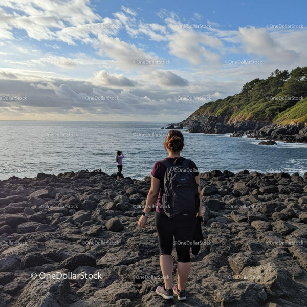 Women Hiking Along Rocky Seaside Coast with Green Hills Under Scenic Sky