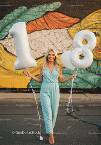Smiling woman celebrating with white balloons outdoors