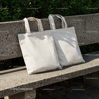 Two Blank Canvas Tote Bags on Outdoor Concrete Bench