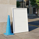Blank white frame resting next to blue traffic cone outdoors