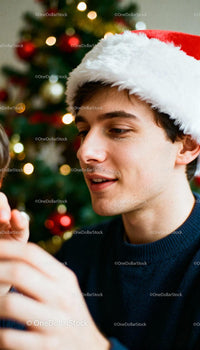Young man wearing Santa hat decorating Christmas tree
