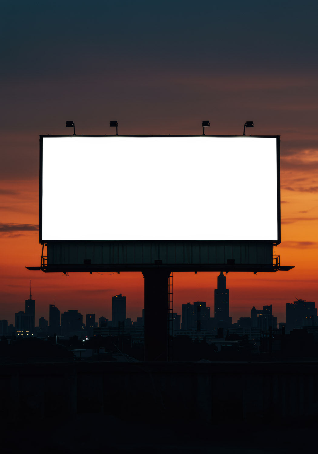 Pusty billboard świecący na tle panoramy miasta o zachodzie słońca
