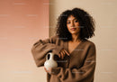 Young Woman in Brown Sweater with Curly Hair Holding a Cream Vase