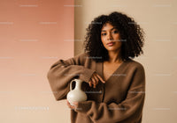 Young Woman in Brown Sweater with Curly Hair Holding a Cream Vase