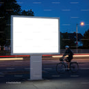 Cyclist passing by illuminated blank billboard at night