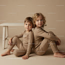 Two children sitting back to back in beige outfits