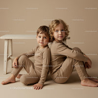 Two children sitting back to back in beige outfits