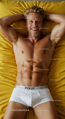 Smiling muscular man relaxing on yellow bed linen