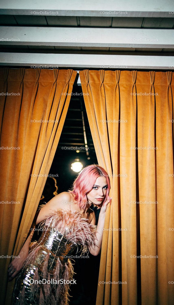 Fashionable woman with pink hair peeking through curtains