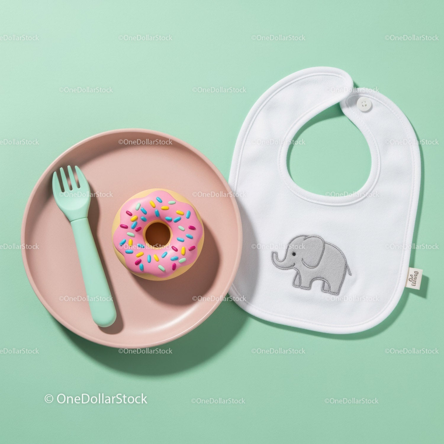 Baby feeding set with toy donut and bib on green table
