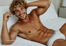 Smiling muscular man relaxing on white bed in underwear