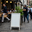 Blank sidewalk sign outside busy urban cafe