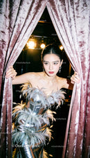 Elegant woman in feathered silver dress behind velvet curtains