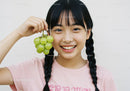 Joyful Girl with Braided Hair Holding Green Grapes in Bright Setting