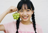 Joyful Girl with Braided Hair Holding Green Grapes in Bright Setting