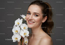 Portrait of a Smiling Woman with White Orchid Flower on Gray Background