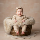 Adorable baby girl sitting in woven basket with fur
