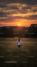 Woman walking in tall grass towards glowing sunset
