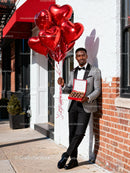 Elegant man holding heart balloons and chocolates outdoors