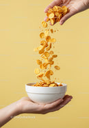 Hand pouring cornflakes into white bowl over yellow background