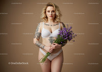 Beautiful Tattooed Woman in White Lingerie Holding Purple Flowers with Beige Background