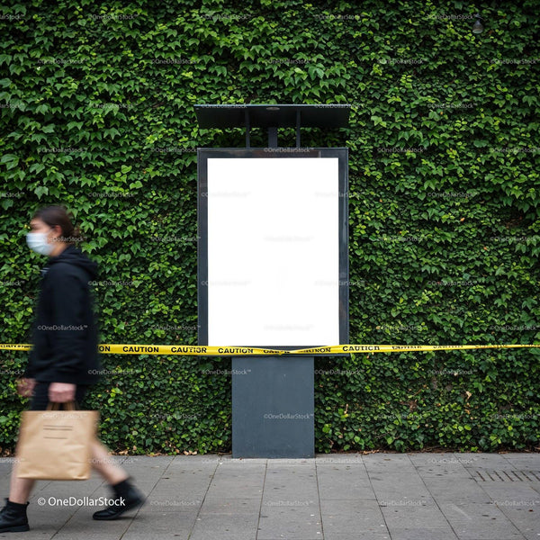 Masked pedestrian walking past blank urban billboard with caution tape JPG Mockup Image